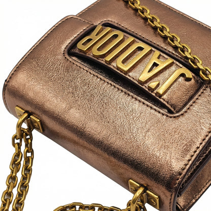 Quartz — A compact flap-style crossbody bag with a chain strap and metal accent.